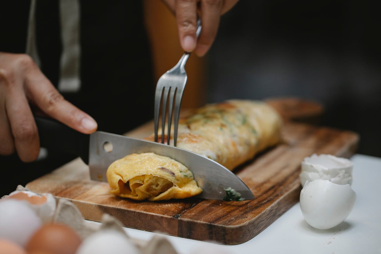 Crop anonymous cook with knife and fork cutting yummy hot egg roll on wooden board